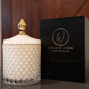  A luxurious white-patterned Wix and Vibes candle jar with a golden crown lid, placed beside its elegant black packaging box with the brand's logo in gold. sexy candles. masculine candles. black owned candle company. 