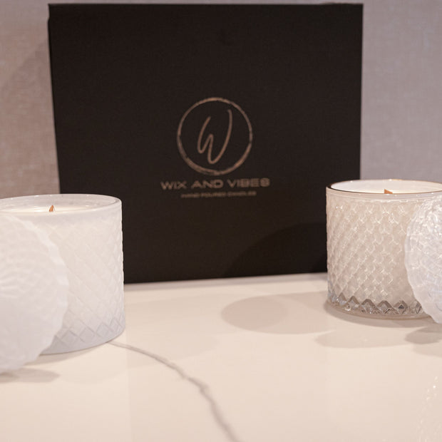 Two luxurious Wix and Vibes candle jars, one shiny white and one matte white, displayed in an elegant black box with a branded lid and rechargeable flameless ligher. sexy candles. Crown collection masculine candles. black owned candle company.